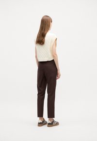 Cream cable-knit sleeveless sweater paired with high-waisted brown trousers and brown sneakers with white accents. Rear view of outfit.