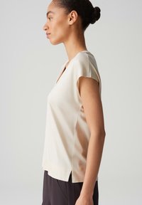 Lichtbeige T-shirt met korte mouwen, een V-hals en zijsplitten, gemaakt van een gladde stof. Het heeft een relaxte pasvorm en een eenvoudig ontwerp.