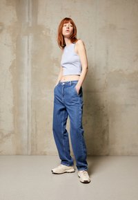 Lys blå crop topp, avslappede blå denimjeans og beige sneakers med detaljer. Glatte teksturer, uformelt design og synlige sømmer.