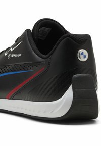 Baskets noires avec semelle blanche, présentant le logo BMW Motorsport, des bandes rouges et bleues, et un détail texturé au talon.