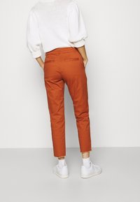 Pantalon en coton orange au design raccourci avec ourlets effilochés. Associé à un pull en maille blanc et des baskets blanches.
