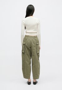 Pulover crem croșetat cu model nervurat, combinat cu pantaloni cargo largi de culoare verde măsliniu, cu buzunare laterale și siluetă relaxată.