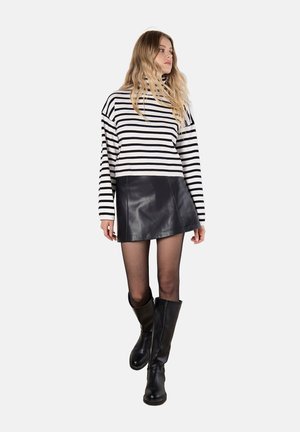 Gestreifter Pulli in Schwarz-Weiß, cropped Design, kombiniert mit einem schwarzen Leder-Minirock und kniehohen schwarzen Stiefeln, Beine in schwarzen Strumpfhosen.