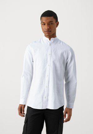 Cămașă albă cu mâneci lungi și guler mandarin, fabrică ușoară și textură subtilă, asortată cu pantaloni cargo negri.