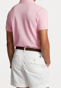 Rosa kortärmad polo med krage, i kombination med vita shorts med knäppta bakfickor och en liten logotyp nära midjan.