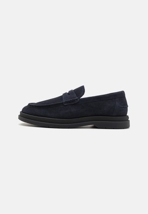 Mocassin en daim bleu foncé avec semelle noire et couture de style mocassin, vue de côté sur fond blanc.
