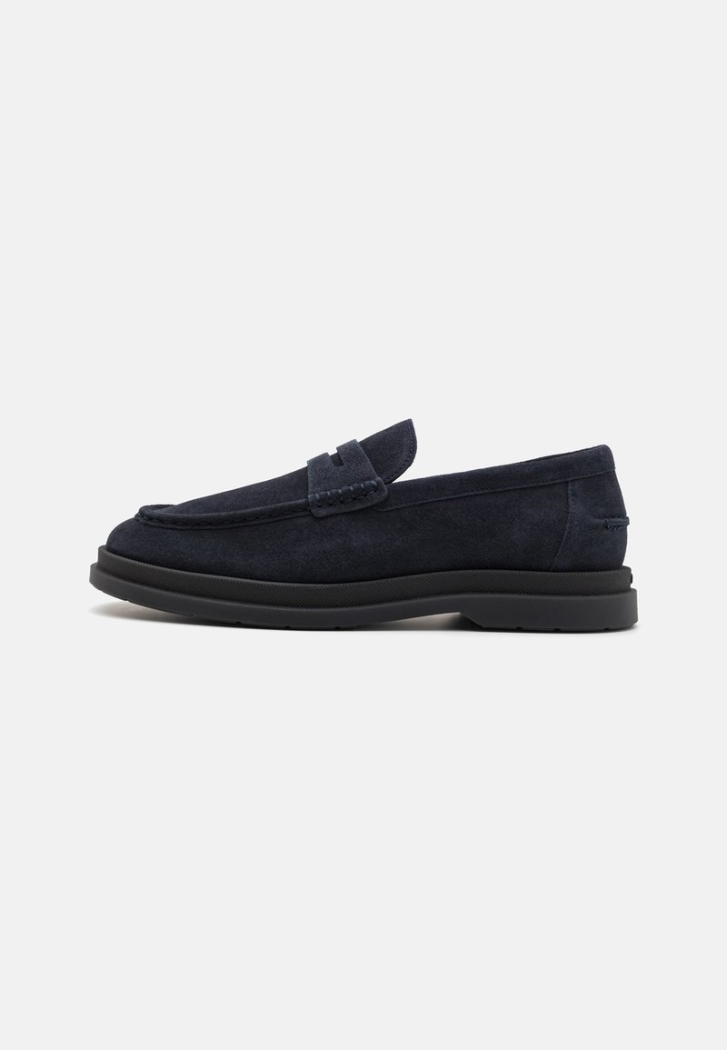 Mocassin en daim bleu foncé avec semelle noire et couture de style mocassin, vue de côté sur fond blanc.