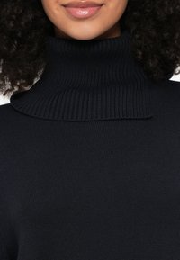 Camisola de gola alta azul-marinho com textura canelada e design de gola dobrável, apresentando tecido suave e ajuste justo.