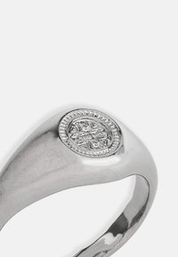 Ezüst gyűrű sima, fényes szalaggal és ovális formájú díszes kerettel, amely körül bonyolult mintázat található egy középső motívum körül.