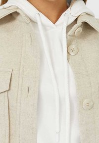 Beige wollen jack van een wolmix met twee knopen, zijzakken, en een lichtgekleurde hoodie met een koord. Zachte textuur en gelaagd ontwerp.
