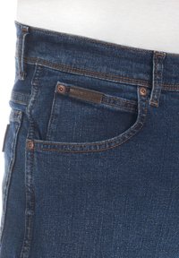 Jeans de mezclilla azul oscuro con una textura suave, con costuras naranjas, un bolsillo delantero y una pequeña etiqueta de cuero en la cinturilla.
