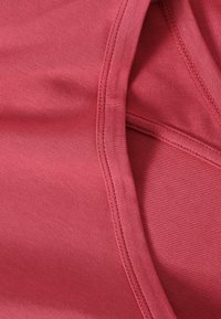 Gros plan sur un tissu rose montrant les surpiqûres détaillées et la structure des coutures d'un vêtement, mettant en avant la texture et la qualité de la couture.