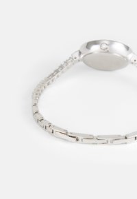 Orologio in metallo argentato con un design a bracciale collegato, cassa circolare, superficie liscia e dettagli minimalisti sul cinturino.
