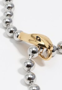 Srebrny metalowy łańcuszek na szyję z złotym zapięciem w kształcie węża, z czarnym detalem w oku. Gładkie, błyszczące powierzchnie na całej długości.