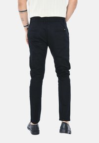 Pantaloni neri slim-fit con passanti per cintura, tasche posteriori e una texture liscia. Abbinati a scarpe nere. Sfondo bianco.
