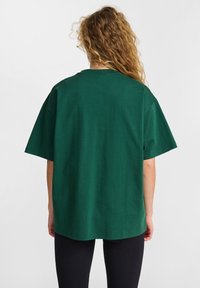 Zielona, oversize'owa koszulka z krótkimi rękawami i okrągłym dekoltem, wykonana z bawełny, o gładkiej fakturze i luźnym kroju.
