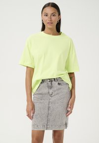 Neon green oversized cotton t-shirt with short sleeves paired with a fitted gray denim skirt featuring a faded texture and front seams.