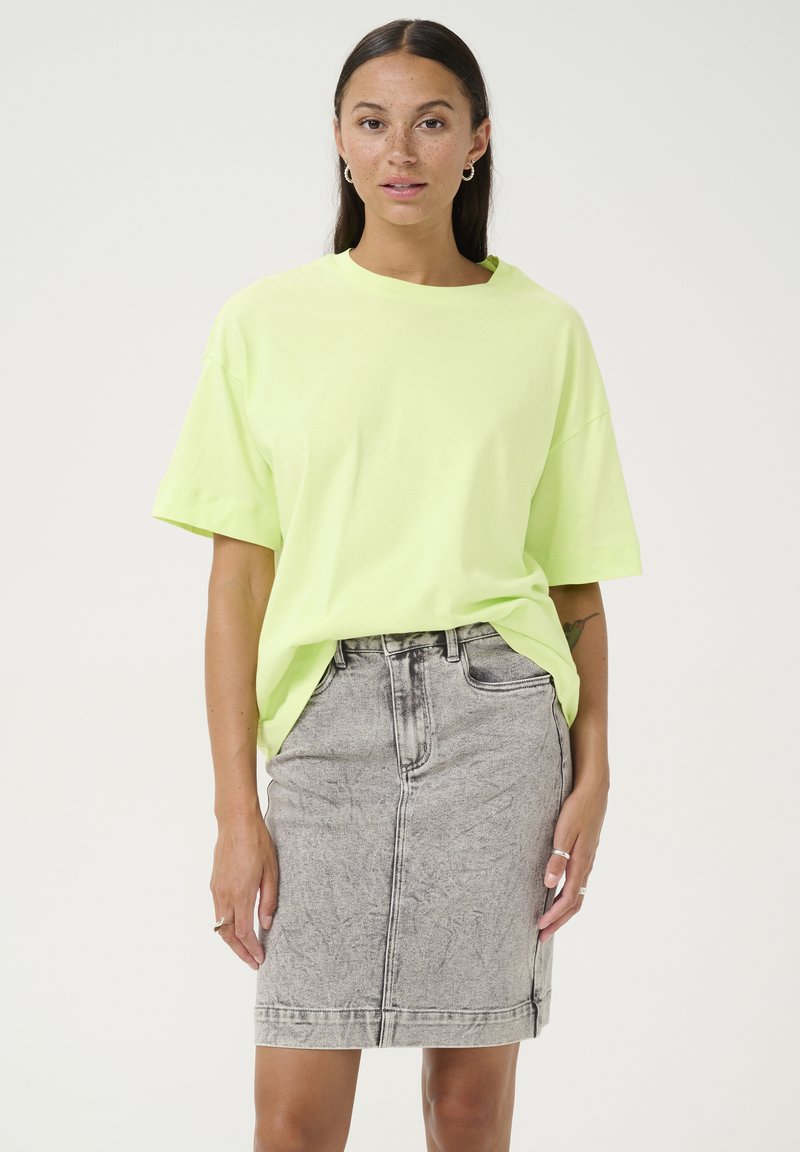 Neon green oversized cotton t-shirt with short sleeves paired with a fitted gray denim skirt featuring a faded texture and front seams.