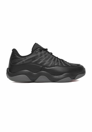 Scarpa da ginnastica nera low-top con tomaia in mesh e pelle, cuciture bianche e suola spessa ondulata in gomma grigia, rivolta verso sinistra.