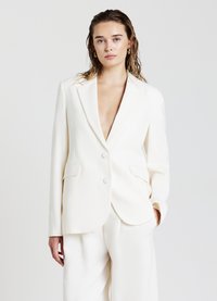 Blazer blanc à double boutonnage avec un décolleté en V profond, deux poches avant et des détails de couture subtils, assorti à un pantalon de la même couleur.