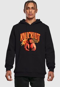 Felpa nera con cappuccio, caratterizzata da un design grafico con guantoni da boxe rossi e la scritta "KNOCKOUT Club" in grassetto con lettering arancione e giallo.
