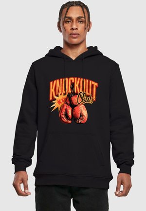 Svart hettegenser med grafisk design som viser røde boksehansker og teksten "KNOCKOUT Club" i fet oransje og gul skrift.