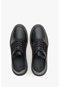 Černé tenisky s hladkým koženým špičkou, semišovými stranami, perforovaným designem a černými tkaničkami. Texturovaná podešev zajišťuje přilnavost.