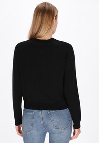Pulover negru u�șor, cu mâneci lungi, decolteu rotund și tiv cu elastic. Vedere din spate arată o textură netedă și o siluetă ajustată.