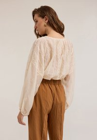 Bluză crem din țesătur�ă texturată, cu broderie florală, asociată cu pantaloni plisati de culoare ruginie, cu talie elastică.