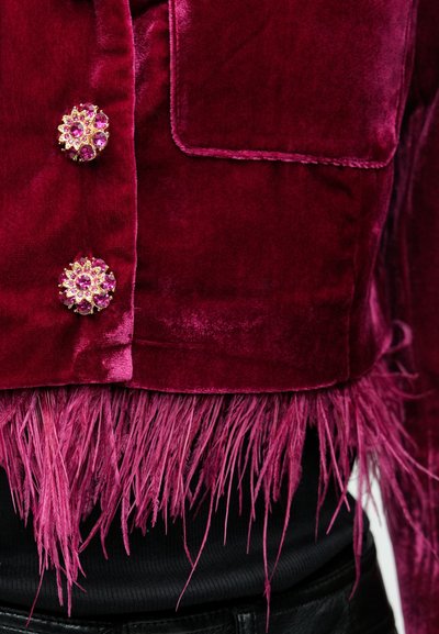 Burgundi sametist jakk kahe roosade lillekujulise kivikestega nupu, millel on tuttidega serv ja sile tekstuur. All must soonikkoega top.