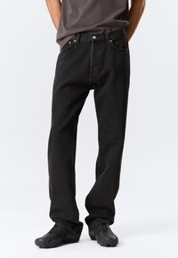 Jeans de mezclilla negra con un corte recto clásico. Presenta cinco bolsillos, un cierre de botón y remaches de cobre contrastantes. Tejido texturizado.