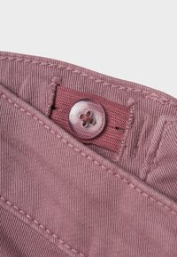 Tessuto di cotone rosa con chiusura a bottone e vita cucita, caratterizzato da una trama sottile a coste e da un dettaglio circolare del bottone.