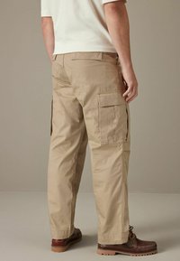 Beige cargo bukser med flere sidelommer, tapered ben design og en tekstureret stof. Båret med brune loafers.