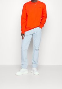 Oranžová mikina, světle modré džíny a bílé tenisky. Mikina má kulatý výstřih a žebrované manžety. Džíny mají rovný střih.