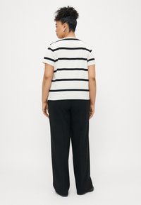 Fekete vízszintes csíkokkal díszített fehér póló, rövid ujjú, kerek nyakkivágással, laza fekete nadrággal párosítva. Egyszerű dizájn, sima textúra.