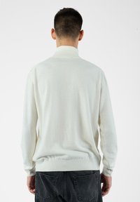 Jasno-beżowy sweter z dzianiny z wysokim kołnierzem, prążkowanymi mankietami i pasem. Miękka struktura i luźny krój. Przedstawiony widok z tyłu.