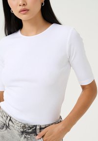 White ribbed short-sleeve top with a round neckline, paired with high-waisted faded grey jeans. Simple design with a fitted silhouette.