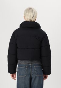 Sort cropped puffer-jakke med høj krave, der har quiltede sektioner og en glat tekstur. Kombineret med mid-blue denim jeans.