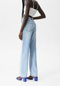 Lichtblauwe wijdvallende spijkerbroek van denim, met achterzakken, gecombineerd met blauwe sandalen met blokhak. Textuurstof met een casual pasvorm.