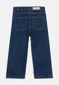 Pantalones vaqueros de pierna ancha de color azul oscuro con dos bolsillos traseros y una etiqueta blanca con el texto naranja "TINY" en la cinturilla.