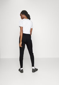 Witte shirt met korte mouwen en grijze accenten, gecombineerd met zwarte, taps toelopende broek met zijstripes. Model draagt zwarte sportschoenen en sokken.