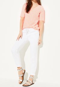 Camisa de manga corta en rayas de color coral y blanco con escote en V, pantalones blancos ajustados, y sandalias plateadas de tiras con suela plana.