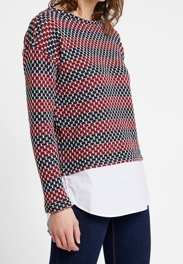 Haut à manches longues en maille avec un motif texturé en rouge, marine et blanc. Look superposé avec un ourlet blanc et un col arrondi.