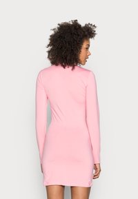 Vestido rosa de manga longa com um design ajustado. Tecido suave e elástico com um fecho atrás. Comprimento até à coxa e silhueta simples.
