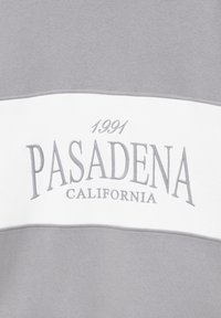 Tissu gris et blanc avec "1991 PASADENA CALIFORNIA" brodé en fil gris sur la partie blanche.