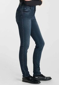 Jean slim-fit bleu marine en denim, avec une taille mi-haute, un design classique à cinq poches, et une texture lisse avec un décoloration minimale.