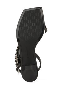 Melnas sandaļu zole ar strukturētu virsmas rakstu. Satur dekoratīvas pērlītes un metāla akcentus uz siksniņas. Izmērs norādīts kā 39.