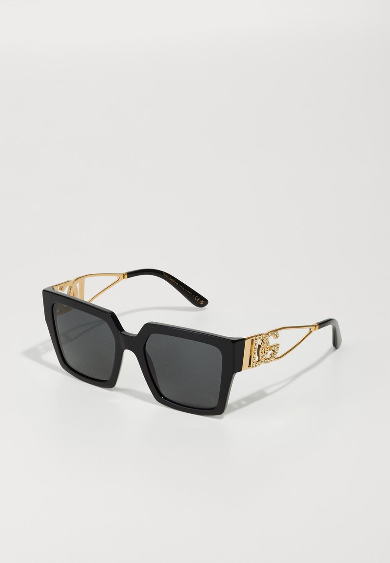 Óculos de sol quadrados oversized pretos com lentes cinzas. Acentos em metal dourado nas hastes, apresentando detalhes de logótipos adornados com pequenas tachinhas.