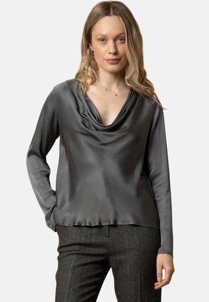 Blusa grigia in satin a maniche lunghe con scollatura drappeggiata, texture liscia e vestibilità rilassata, abbinata a pantaloni a righe.