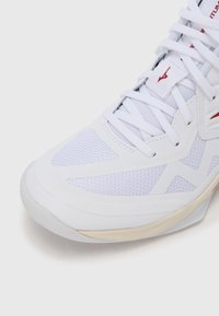 Λευκό αθλητικό παπούτσι με πλέγμα στο επάνω μέρος, καουτσούκ σόλα και περίπλοκες λεπτομέρειες. Διαθέτει επίπεδα κορδόνια και χαρακτηριστική σήμανση στη γλώσσα.